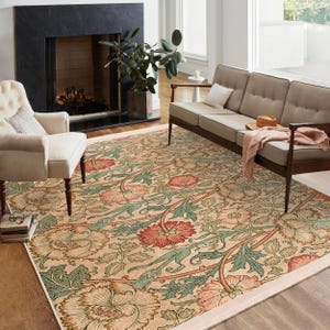 May include: A beige area rug with a floral pattern featuring pink, green, and brown tones. The rug has a white border and is shown in a living room setting.