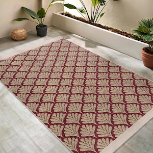May include: A rectangular area rug with a repeating pattern of beige fan-like shapes on a burgundy background. The rug has a cream-colored border and is placed on a light-colored surface. The rug is a decorative element for indoor or outdoor spaces.