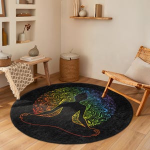 Op de afbeelding: Een rond, zwart vloerkleed met een kleurrijk mandala-ontwerp met een silhouet van een persoon in een yogapose. De mandala is gemaakt van ingewikkelde patronen in tinten rood, oranje, geel, groen, blauw, indigo en violet.