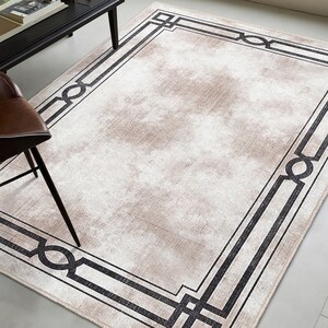 May include: A beige area rug with a black geometric border. The border is made up of repeating squares and circles.