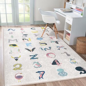 Op de afbeelding: Een wit tapijt met een kleurrijk alfabetontwerp met dieren. Elke letter van het alfabet wordt gevormd door een dier, zoals een flamingo, een zebra en een octopus.