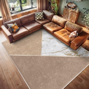 May include: A brown and white area rug with a geometric design. The rug has a beige background with a white marble pattern in the centre and a brown leopard print pattern in the top left corner. The rug is on a hardwood floor in a living room with a brown leather sectional sofa.