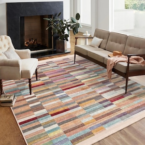 May include: A multi-colored area rug with a geometric pattern of horizontal and vertical stripes in shades of brown, red, blue, green, and pink. The rug is laid out in a living room with a fireplace and a sofa.