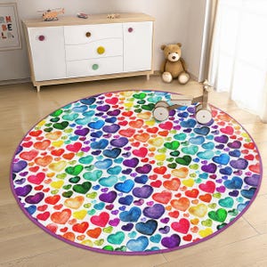 May include: A round, colorful play rug with a white background and a pattern of rainbow-colored hearts. The rug has a purple border.