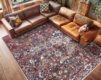 May include: An overhead shot of a living room featuring a large, brown leather sectional sofa and a patterned area rug. The rug has a red, blue, and cream floral design. The room has hardwood floors and natural light from a large window.