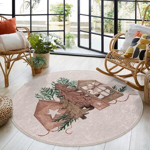 Könnte beinhalten: Ein runder, cremefarbener Teppich mit einem verspielten Design, das einen stilisierten Baum mit braunen Ästen und grünen Blättern zeigt. Der Baum ist von kleinen, braunen Häusern mit weißen Akzenten und einem Stern umgeben.