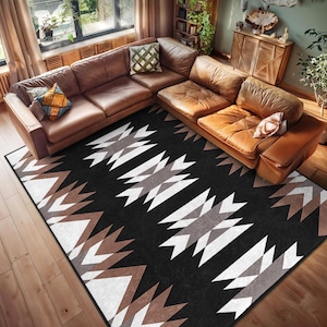Puede incluir: Una alfombra geométrica en blanco y negro con acentos marrones. La alfombra tiene un patrón tribal y se coloca en una sala de estar con un sofá seccional de cuero marrón.