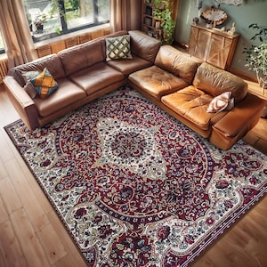 Puede incluir: Una alfombra de salón de color burdeos y crema con un diseño floral. La alfombra está colocada sobre un suelo de madera dura en un salón con un sofá de cuero marrón.