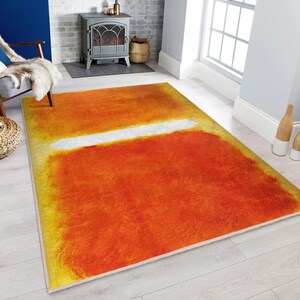 Puede incluir: Alfombra de arte abstracto con un esquema de color amarillo, naranja y blanco. La alfombra tiene una franja horizontal blanca en el medio.