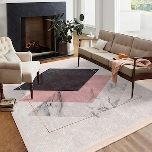 Puede incluir: Una alfombra moderna de estilo geométrico con fondo blanco, formas geométricas negras y rosas y detalles dorados. La alfombra está en un salón con un sofá y una chimenea.