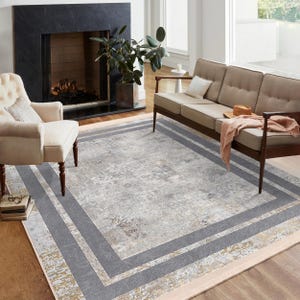 May include: A grey and beige area rug with a distressed pattern and a multi-coloured border. The rug has a light pink inner border, two grey borders, and a gold outer border.
