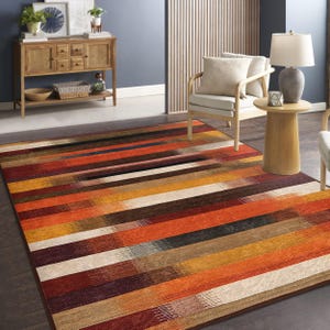 Puede incluir: Una alfombra de área con rayas multicolores en tonos naranja, marrón, rojo y crema. La alfombra está colocada sobre un suelo de madera en un salón.