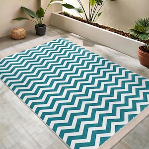 Puede incluir: Alfombra de chevron de color turquesa y blanco con borde blanco. La alfombra está sobre un suelo de madera clara.