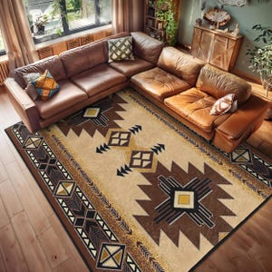 Könnte beinhalten: Ein beiger Teppich mit einem braunen und schwarzen geometrischen Muster. Der Teppich hat ein südwestliches Design mit einer Diamantform in der Mitte und Pfeilen an den Rändern. Der Teppich liegt auf einem Holzboden in einem Wohnzimmer mit einem braunen Ledersofa.