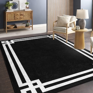 May include: Black and white area rug with a geometric border design. The rug has a white border with a black center.