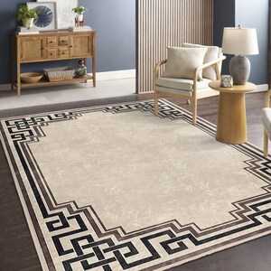 May include: A beige area rug with a black and brown geometric border. The rug has a subtle pattern throughout the center.
