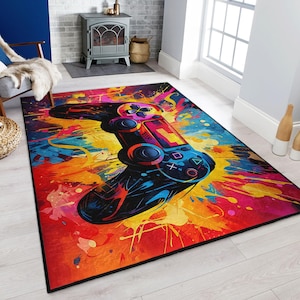 Puede incluir: Una alfombra colorida con un mando de videojuego negro en el centro. El mando está rodeado de salpicaduras de pintura en tonos rojos, naranjas, amarillos, azules y verdes.