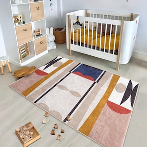 May include: A beige, yellow, red, and blue geometric patterned rug with a white crib in the background.