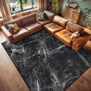 Puede incluir: Una alfombra negra y blanca con un patrón de mármol desgastado. La alfombra está colocada sobre un suelo de madera en un salón con un sofá de cuero marrón.