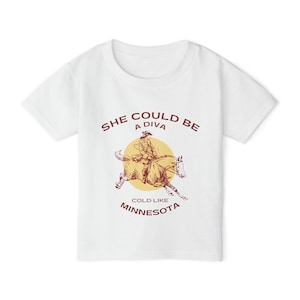 Op de afbeelding: Wit T-shirt met een rode afbeelding van een vrouw die paardrijdt. De tekst luidt "She could be a diva cold like Minnesota".