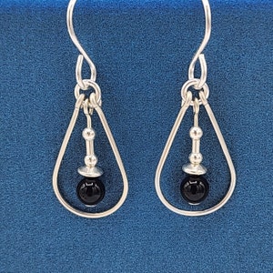 May include: A pair of silver teardrop earrings with black bead accents.