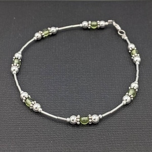 May include: A silver anklet with green glass beads. The anklet has a silver clasp.