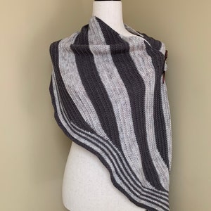 Peut inclure: Un châle en tricot rayé gris et blanc drapé sur un mannequin blanc.