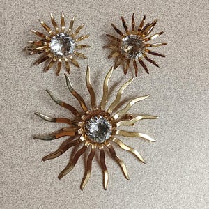 May include: A gold sunburst brooch and matching earrings with clear rhinestone centers.