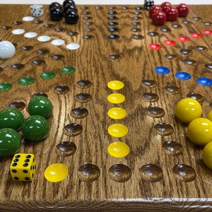May include: Wooden board game with various colored marbles and dice. The game board is made of wood with a natural grain, and the marbles are in shades of green, yellow, blue, red, white, and black. Dice are also included.