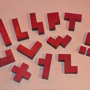 Puede incluir: Un conjunto de 14 piezas de rompecabezas de madera en color rojo oscuro. Las piezas son todas de diferentes formas y tamaños, y están dispuestas en un semicírculo sobre una superficie rosa claro.