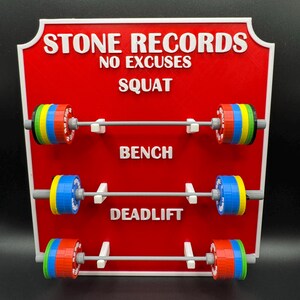 May include: A red sign with white text that reads "STONE RECORDS NO EXCUSES SQUAT BENCH DEADLIFT." The sign has three barbell displays with colorful weight plates. The weights are red, blue, yellow, green, and gray.