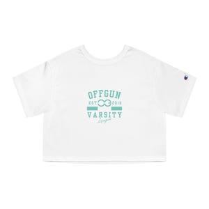 May include: White crop top with the text "OFFGUN EST 2016 VARSITY League" in light blue. The shirt has short sleeves and a crew neck. A small Champion logo is visible on the left sleeve.