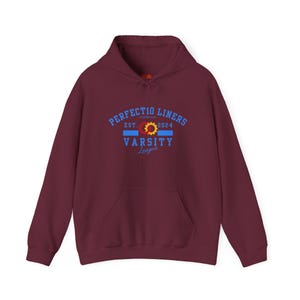 May include: A maroon hoodie with a front pocket and drawstring hood. The front displays the text "PERFECT10 LINERS" above a blue and yellow design, with "EST. 2024" and "VARSITY League" below. The hoodie is made of a soft material.