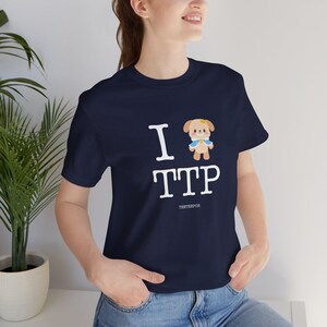 May include: Navy blue t-shirt with the text "I TTP" in white, featuring a cartoon dog illustration. The word "TESTEEFOR" is printed below the text. The shirt is made of a soft material.