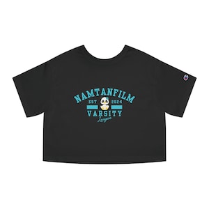 Könnte beinhalten: Schwarzes Crop-Top mit dem Text "NAMTANFILM VARSITY League" in Türkis. Das Design beinhaltet eine Panda-Grafik und das Jahr "2024". Das Shirt ist von der Marke Champion.