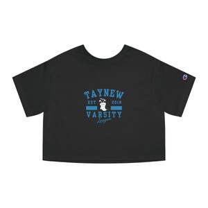 Op de afbeelding: Zwart gecropped T-shirt met een blauwe grafische afbeelding die "Taynew Est 2018 Varsity League" zegt met een spookafbeelding in het midden.