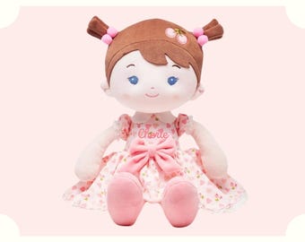 May include: A plush doll with brown hair, blue eyes, and a pink dress with a cherry print. The doll is wearing a pink bow and has the name "Cherie" embroidered on her dress.