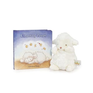 May include: A plush white lamb toy next to a children's book titled "Counting Peeps: A Bedtime Story." The book cover features a sleeping lamb and illustrations of chicks. The lamb toy has a pink nose and small tag.
