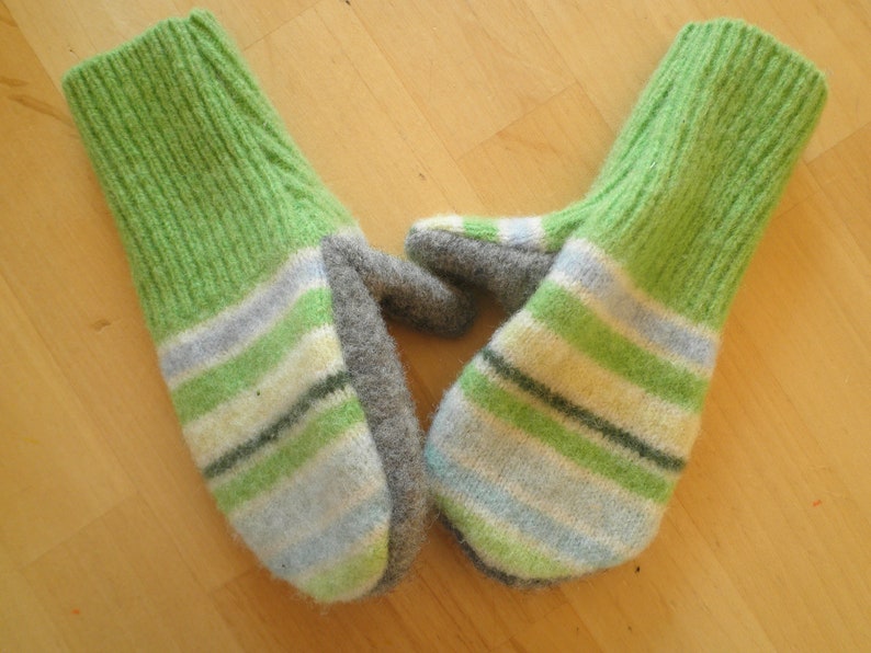 May include: A pair of green and white striped knitted mittens with gray cuffs. The mittens are made of a soft, fuzzy yarn.