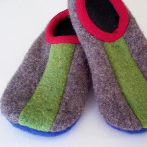 Może przedstawiać: Para szare wełnianych kapci z zielonymi i niebieskimi lamówkami. Kapcie mają czerwoną wstążkę wokół górnej części.