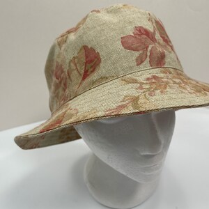 May include: A beige bucket hat with a floral print featuring red and brown flowers. The hat is made of a woven fabric.