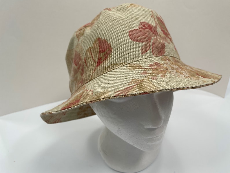 May include: A beige bucket hat with a floral print featuring red and brown flowers. The hat is made of a woven fabric.