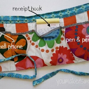 May include: A colorful fabric apron with multiple pockets. The pockets are labeled "cell phone", "receipt book", and "pen & pencils".