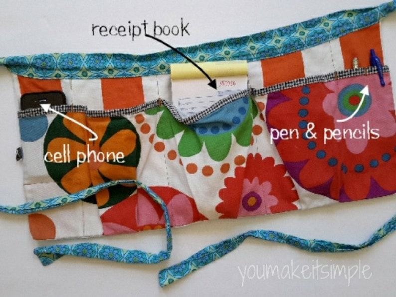 May include: A colorful fabric apron with multiple pockets. The pockets are labeled "cell phone", "receipt book", and "pen & pencils".