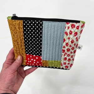 May include: A patchwork fabric zippered pouch with a variety of patterns including floral, polka dot, and geometric designs in red, yellow, black, white, and blue.