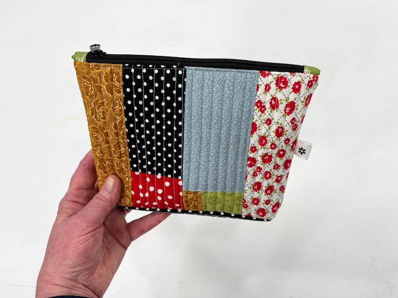 May include: A patchwork fabric zippered pouch with a variety of patterns including floral, polka dot, and geometric designs in red, yellow, black, white, and blue.