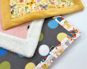 May include: Three different baby blankets with various patterns. One blanket has a yellow floral pattern with a yellow border, another has a pink border with white fur trim, and the last one has a gray background with colorful polka dots and a white border with a cat pattern.