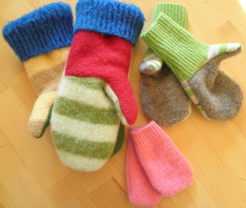 May include: Five pairs of knitted wool mittens in various colors, including green, blue, red, pink, and gray. The mittens are made from recycled wool and have a unique, hand-crafted look.