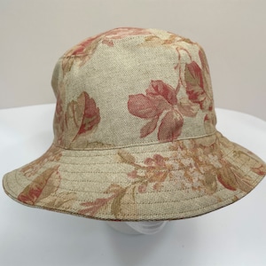 May include: A beige bucket hat with a floral print featuring red and brown flowers. The hat is made of a linen fabric.