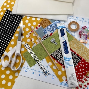 May include: A close-up of a sewing project with various fabrics, tools, and supplies. The fabrics are a mix of patterns, including polka dots, floral, and geometric designs. The tools include scissors, a ruler, a seam ripper, and a zipper. The supplies include a piece of batting, a roll of tape, and a set of fabric clips.